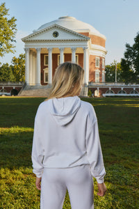 A woman viewed from behind wearing a light gray matching lounge set, standing on a grassy lawn with the historic Virginia domed capitol building in the background.