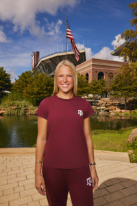 young woman wearing red Texas A&M tee from AVO in front of a pond and stadium