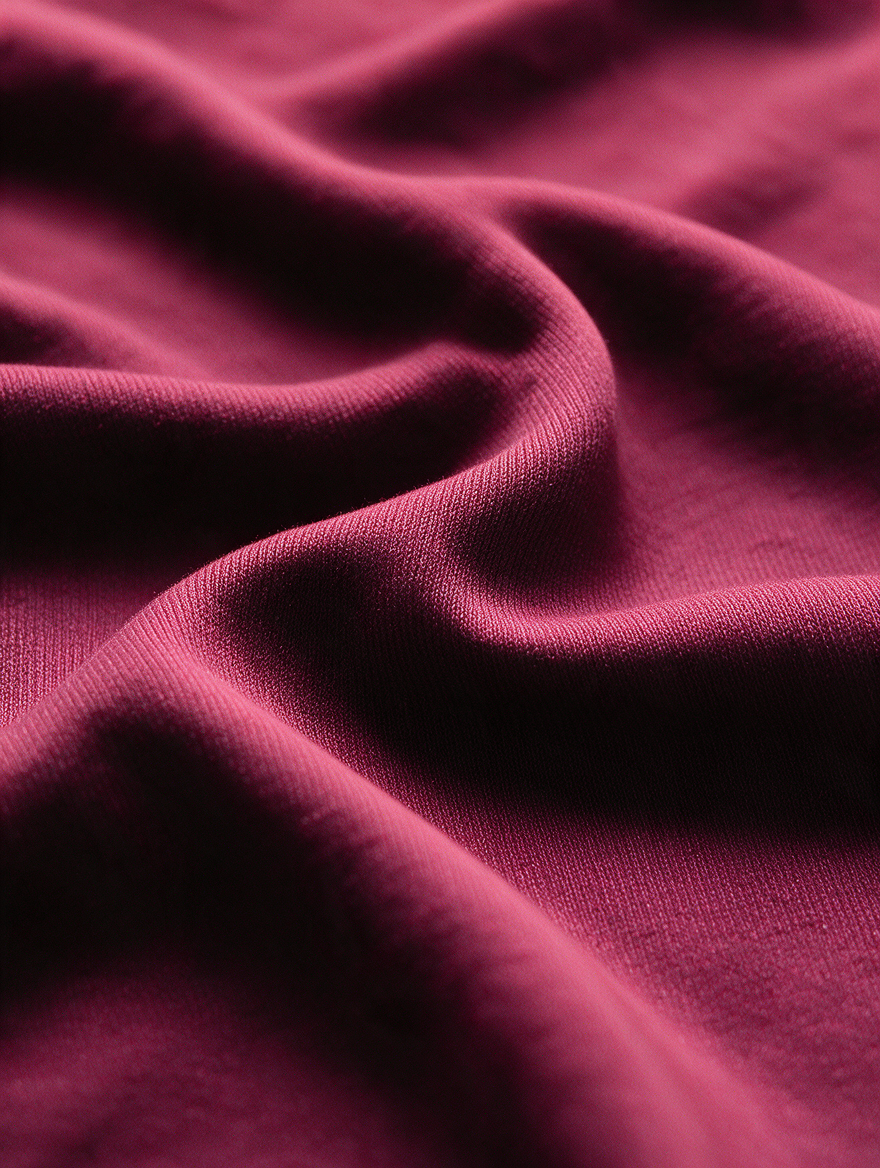 A close-up of draped burgundy fabric with soft folds and visible knit texture.