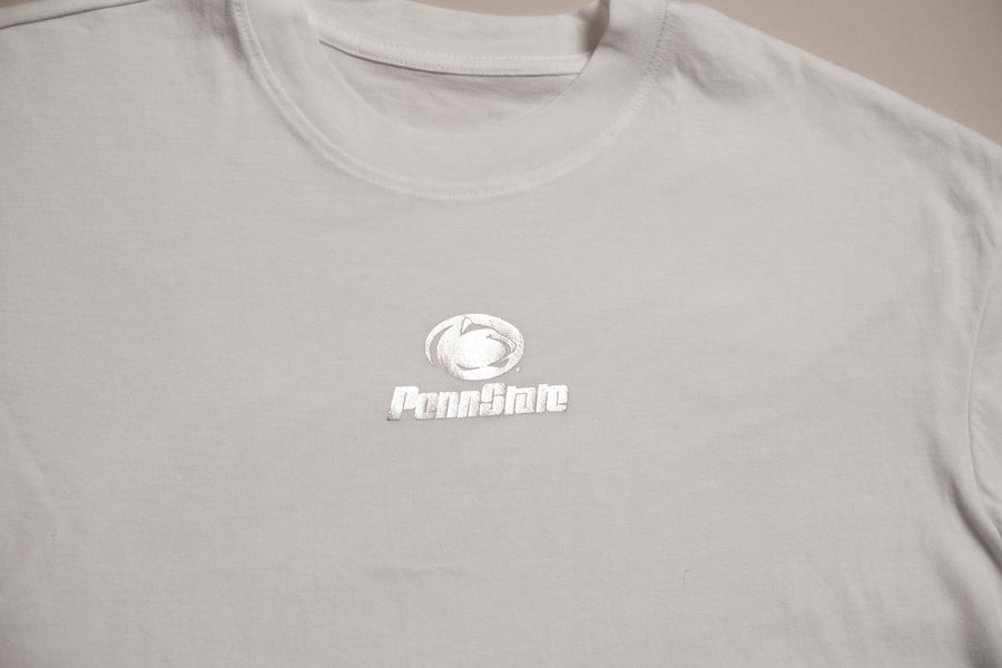 A close-up of a light gray crewneck t-shirt featuring a white printed PennState logo on the center chest.