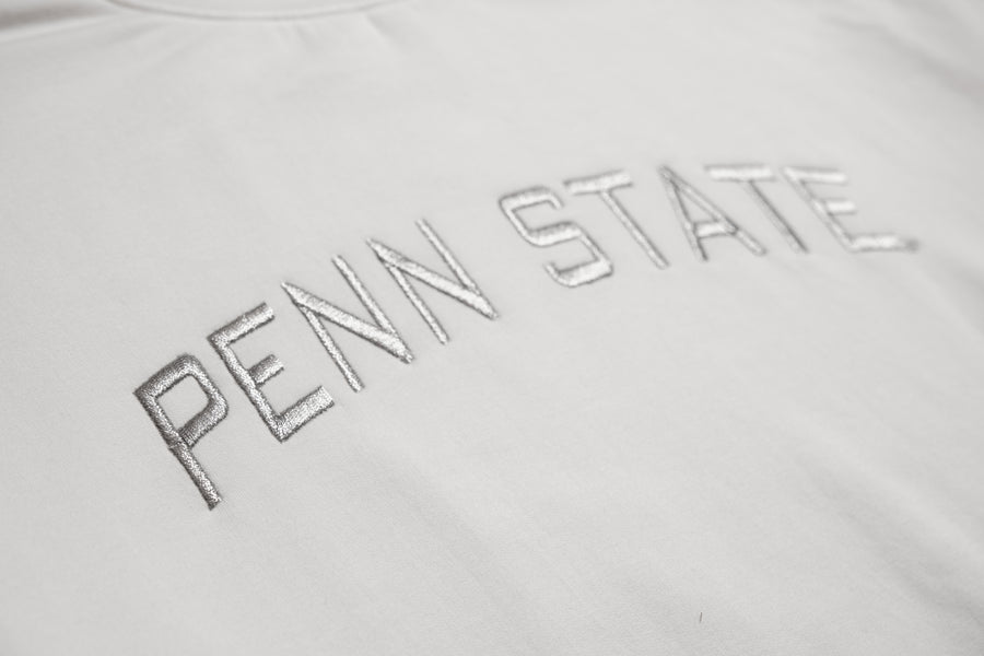Close-up of a white t-shirt featuring metallic silver embroidered 'PENN STATE' text across the chest.