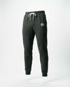 Dark charcoal gray heather sweatpants with a white drawstring and a small white circular logo on the left thigh, shown against a plain white studio background.