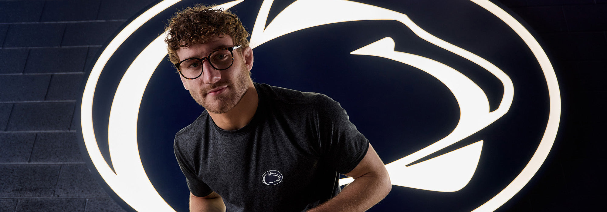 Penn State Wrestler posing in front of logo
